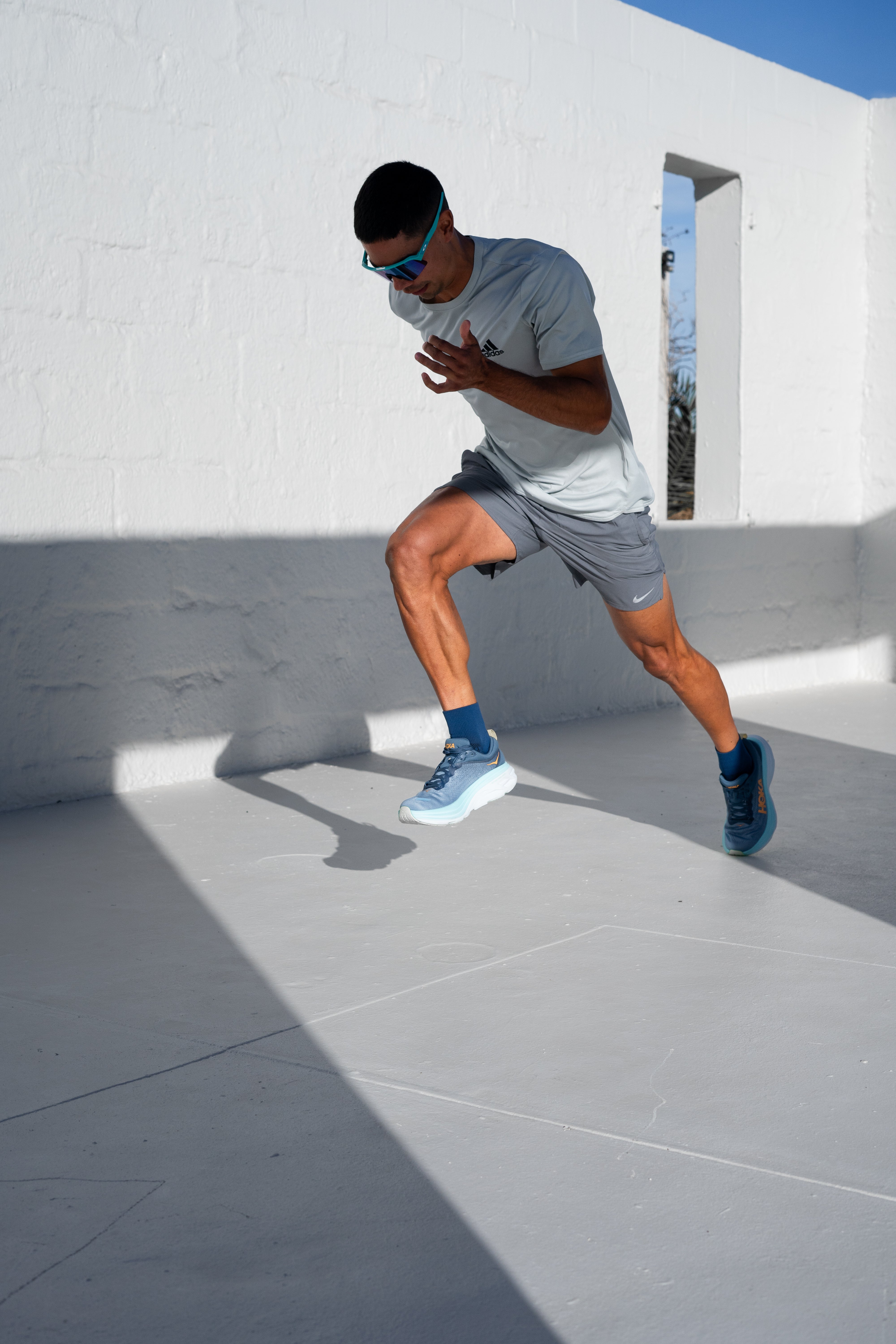Person in athletic wear performing a jog on a rooftop with a white wall and blue sky in the background.